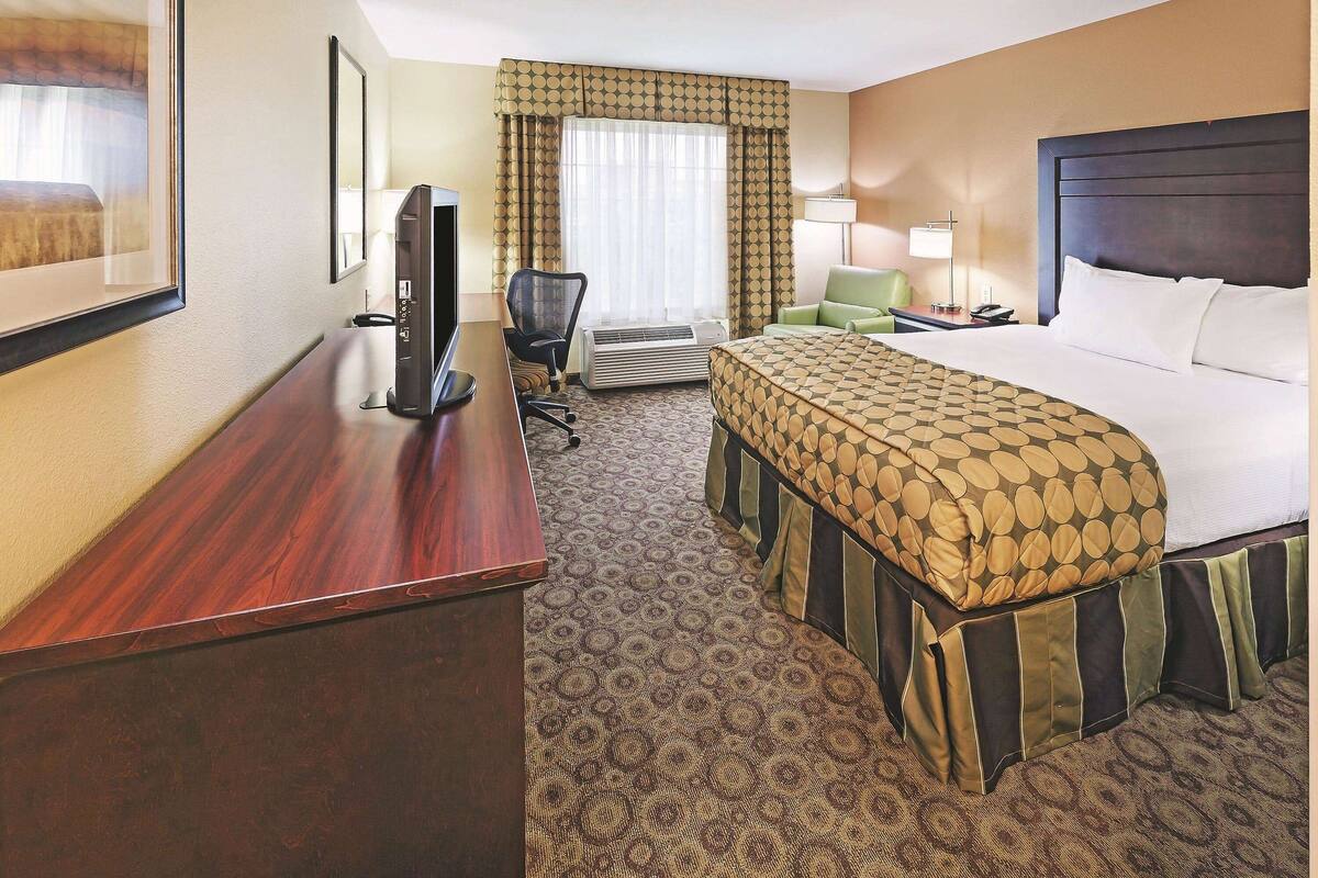 A hotel room with a bed, a desk with a computer, a chair, a lamp, and a window with curtains.