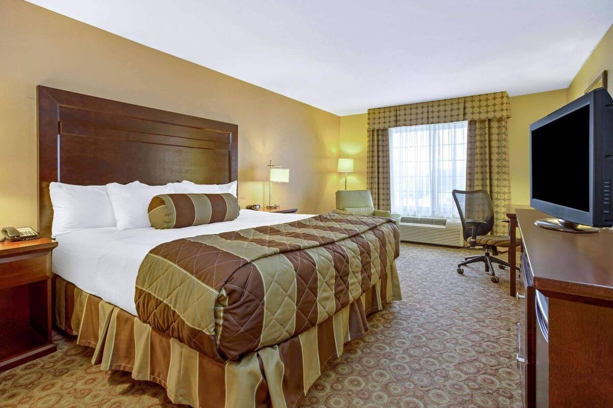 A hotel room with a large bed, a desk with a computer, a television, and a chair.