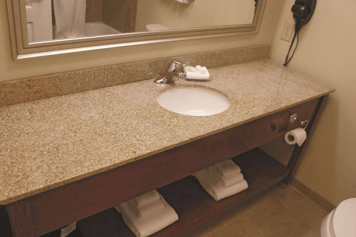 A bathroom with a granite countertop sink, a mirror above it, a towel rack, and a toilet with a paper towel holder.