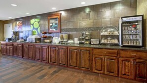Ein Hotel-Rezeptionsbereich mit einer langen Holztresen, einer Kaffeemaschine, einem Getränkeautomaten und einer Obstauslage.