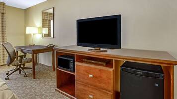 A hotel room with a wooden desk, a television, a microwave, a refrigerator, and a chair.