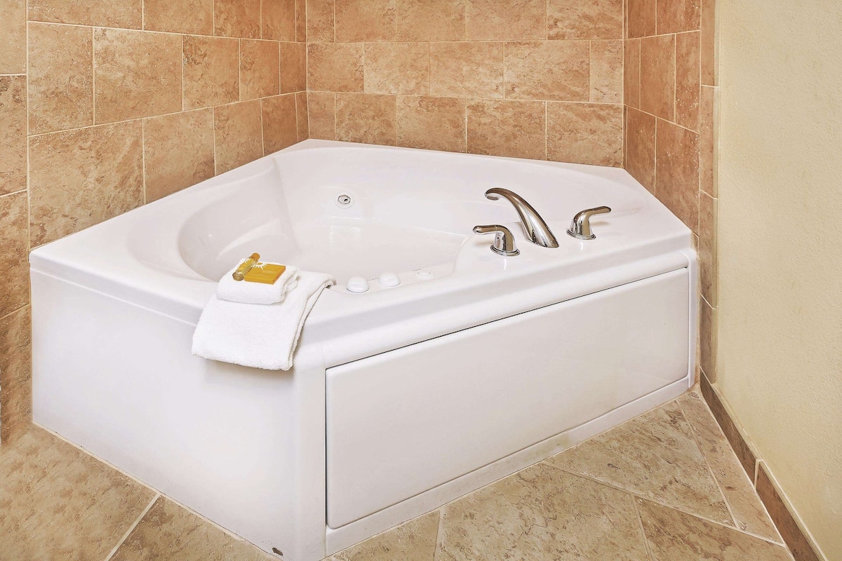 A white bathtub with a single faucet and a control panel, set against beige tiled walls.