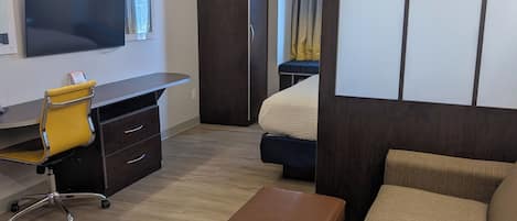 Habitación de hotel con cama, sofá, escritorio con silla, televisor y armario.
