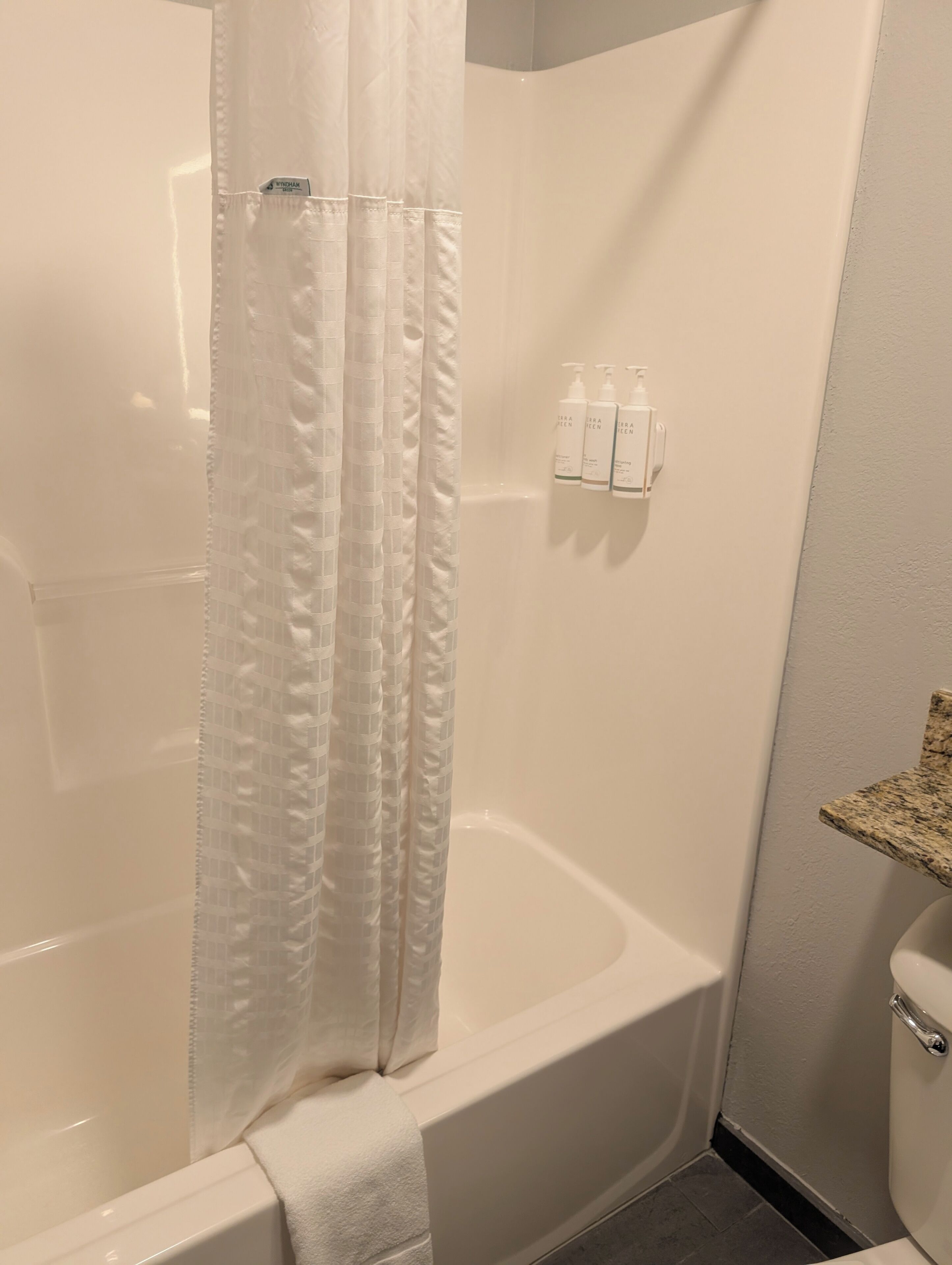 Un baño con una bañera blanca, cortina de ducha y artículos de aseo en un dispensador de pared.
