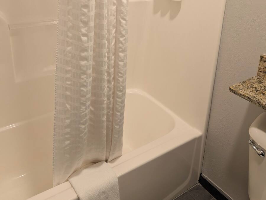 A bathroom with a white bathtub, a shower curtain, and toiletries on a wall-mounted dispenser.