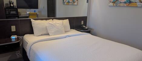 Habitación de hotel con cama, mesita de noche, televisor, cafetera y obras de arte en las paredes.