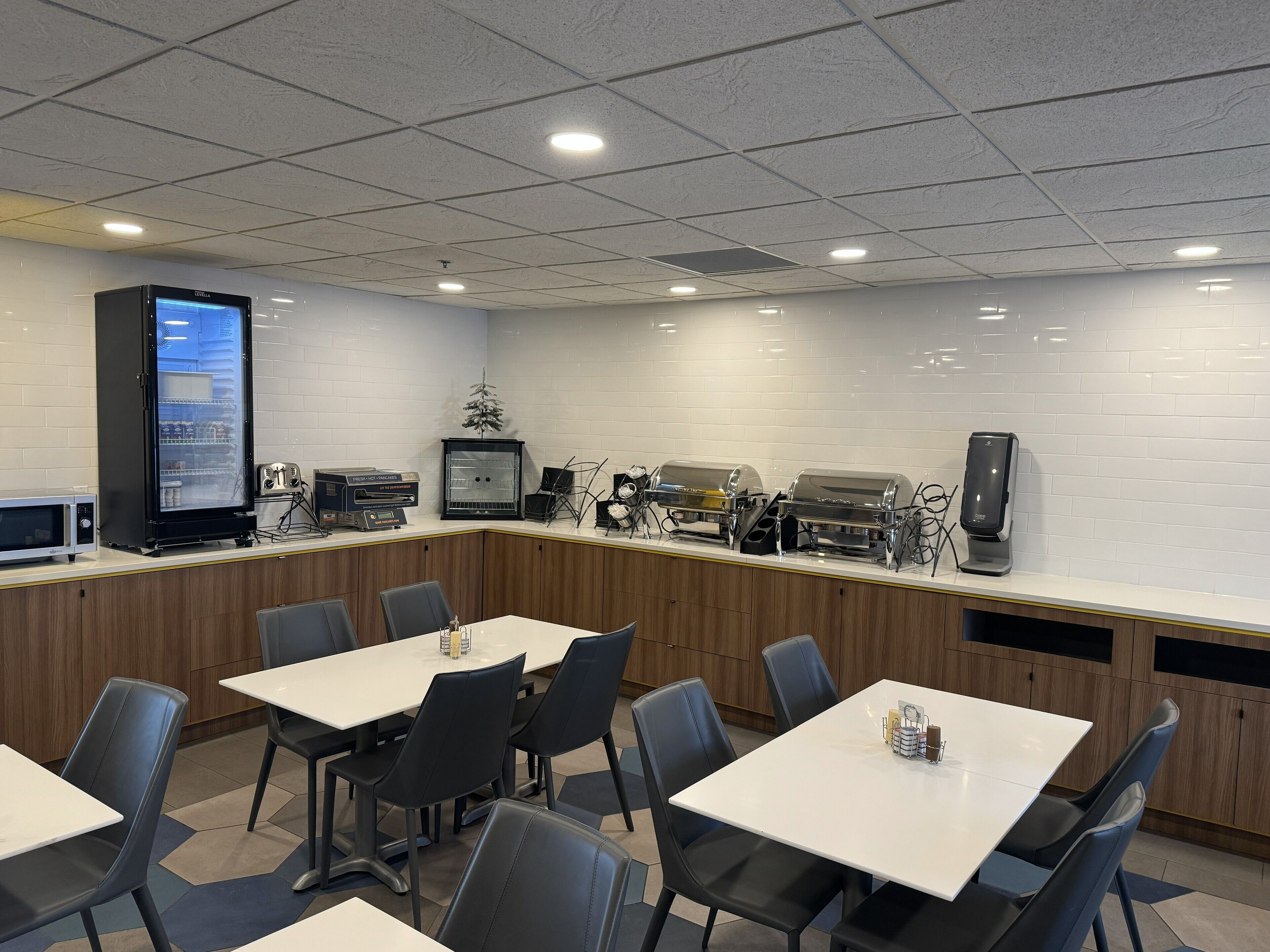 A modern cafe with a long counter, multiple seating tables, and a variety of appliances including a coffee machine and a microwave.