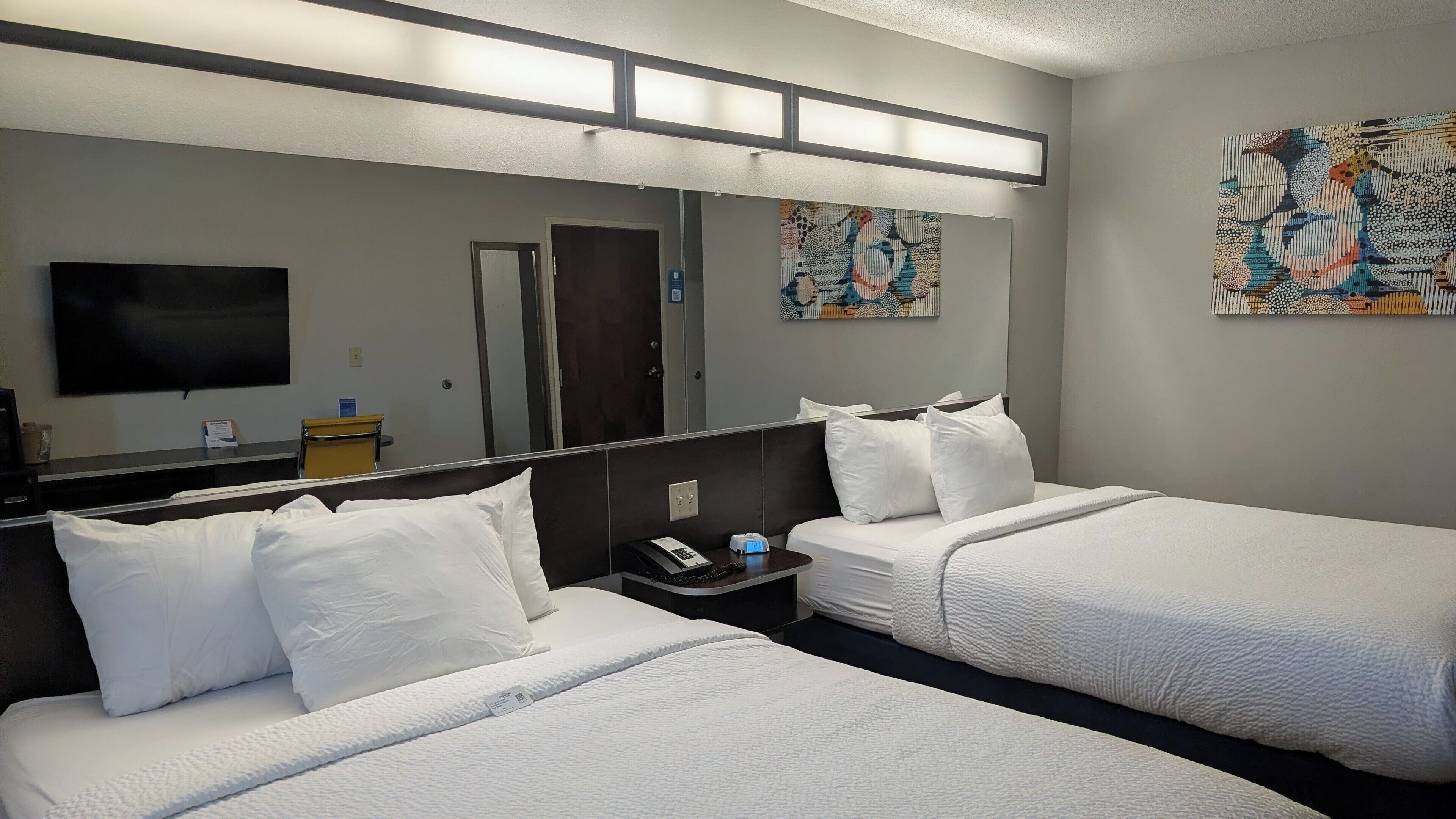 A hotel room with two beds, a TV, a desk, and a mirror.