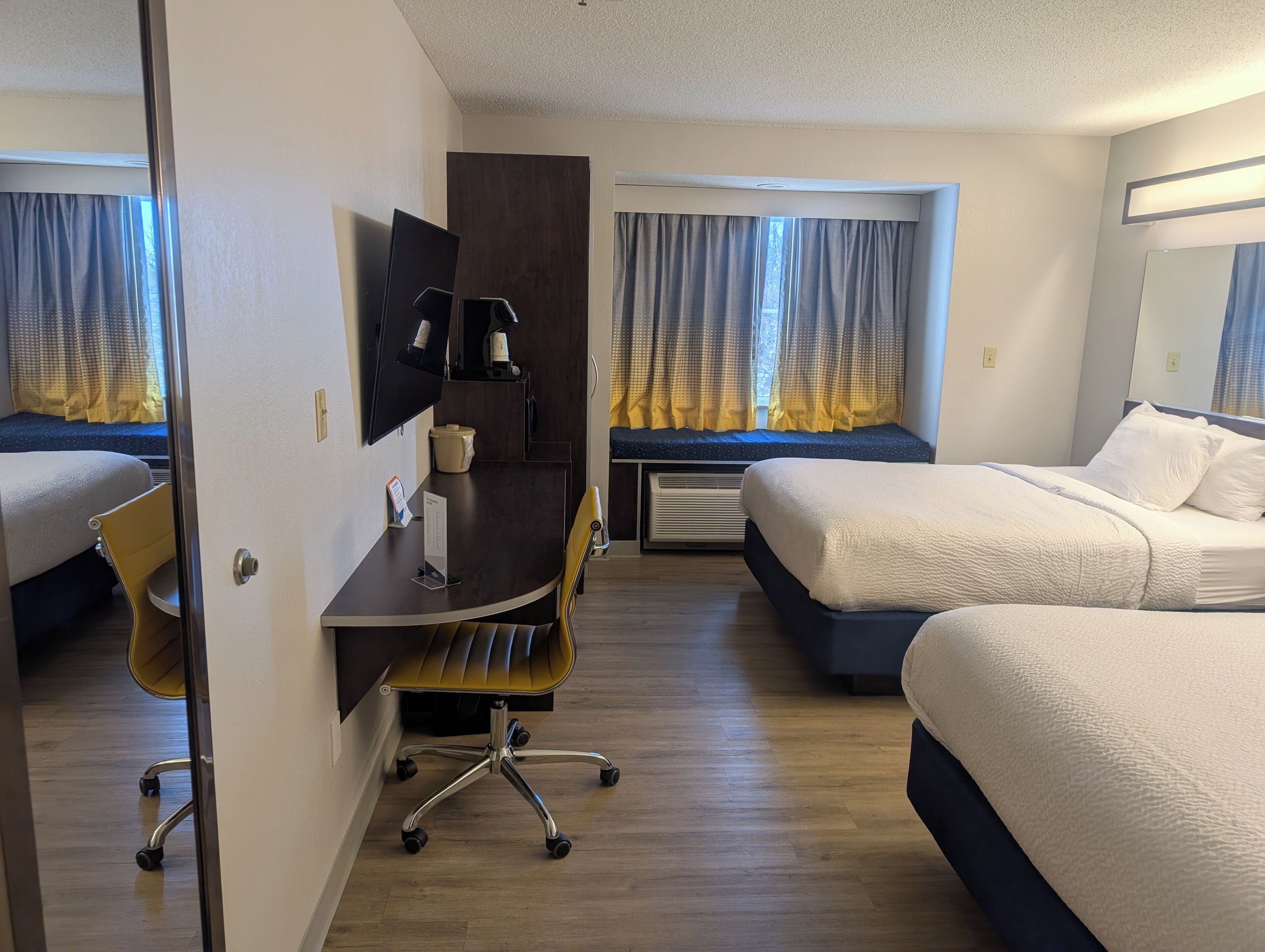 Habitación de hotel con dos camas, un escritorio, una silla, un televisor y una ventana con cortinas.