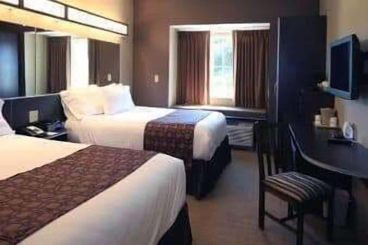 A hotel room with two beds, a desk, a chair, and a television.