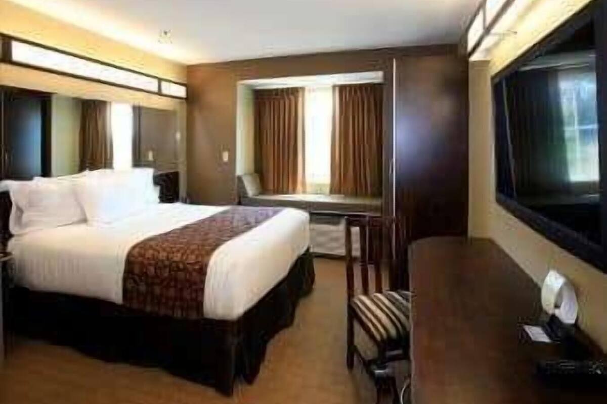 A hotel room with a large bed, a desk, a chair, a TV, and a window with curtains.