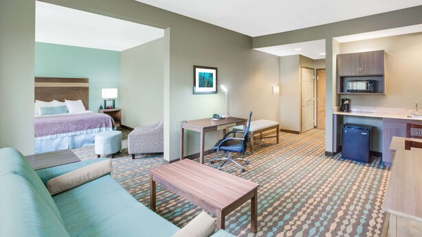 A hotel room with a bed, a desk, a chair, a sofa, a small table, a microwave, and a kitchenette. - Wingate by Wyndham Bossier City, LA (Bossier City)