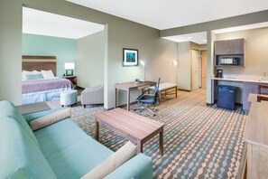 Habitación de hotel con cama, escritorio, silla, sofá, mesita pequeña, microondas y kitchenette.