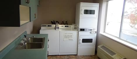 A laundry facility with stacked washers and dryers, a sink, and a window with a view of trees.