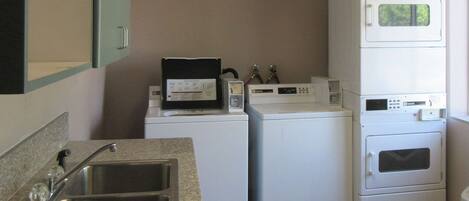 A laundry area with a sink, stacked washer and dryer, and a microwave.