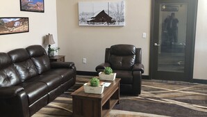 A living room with a brown leather sofa, a brown leather armchair, and a wooden coffee table with a plant. There is a framed picture of a barn on the wall. - Quality Inn Spanish Fork North (Spanish Fork)