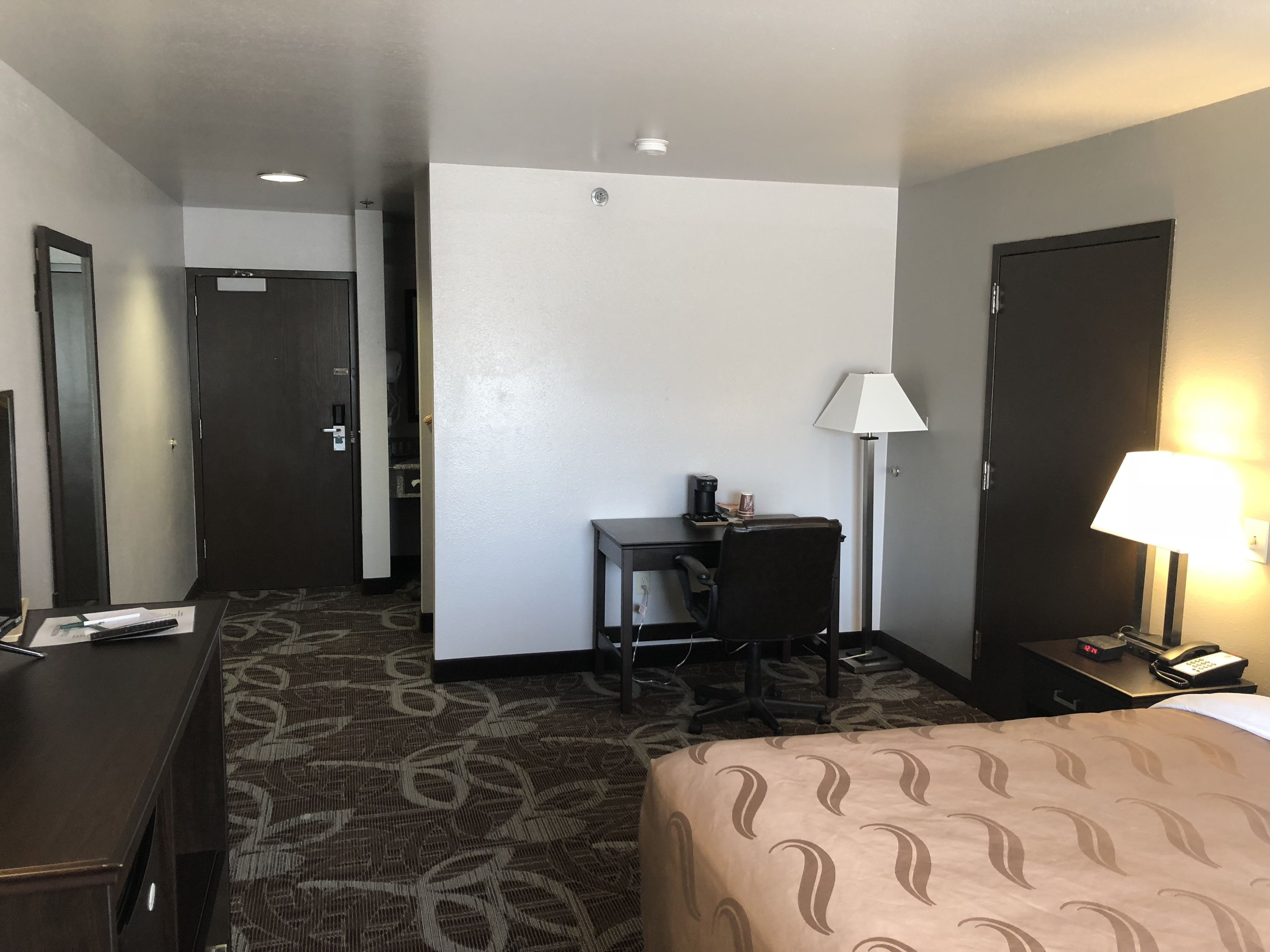 Una habitación de hotel con una cama, un escritorio con una silla, una lámpara y un teléfono.