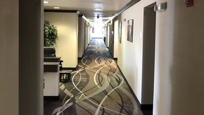 A hotel hallway with an exit sign, a reception desk, a plant, and framed pictures on the walls. - Quality Inn Spanish Fork North (Spanish Fork)