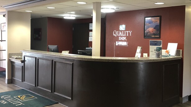 A hotel reception desk with a dark counter, a computer, and a sign that reads "Quality Inn." - Quality Inn Spanish Fork North (Spanish Fork)