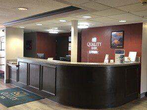 A hotel reception desk with a dark counter, a computer, and a sign that reads "Quality Inn." - Quality Inn Spanish Fork North (Spanish Fork)
