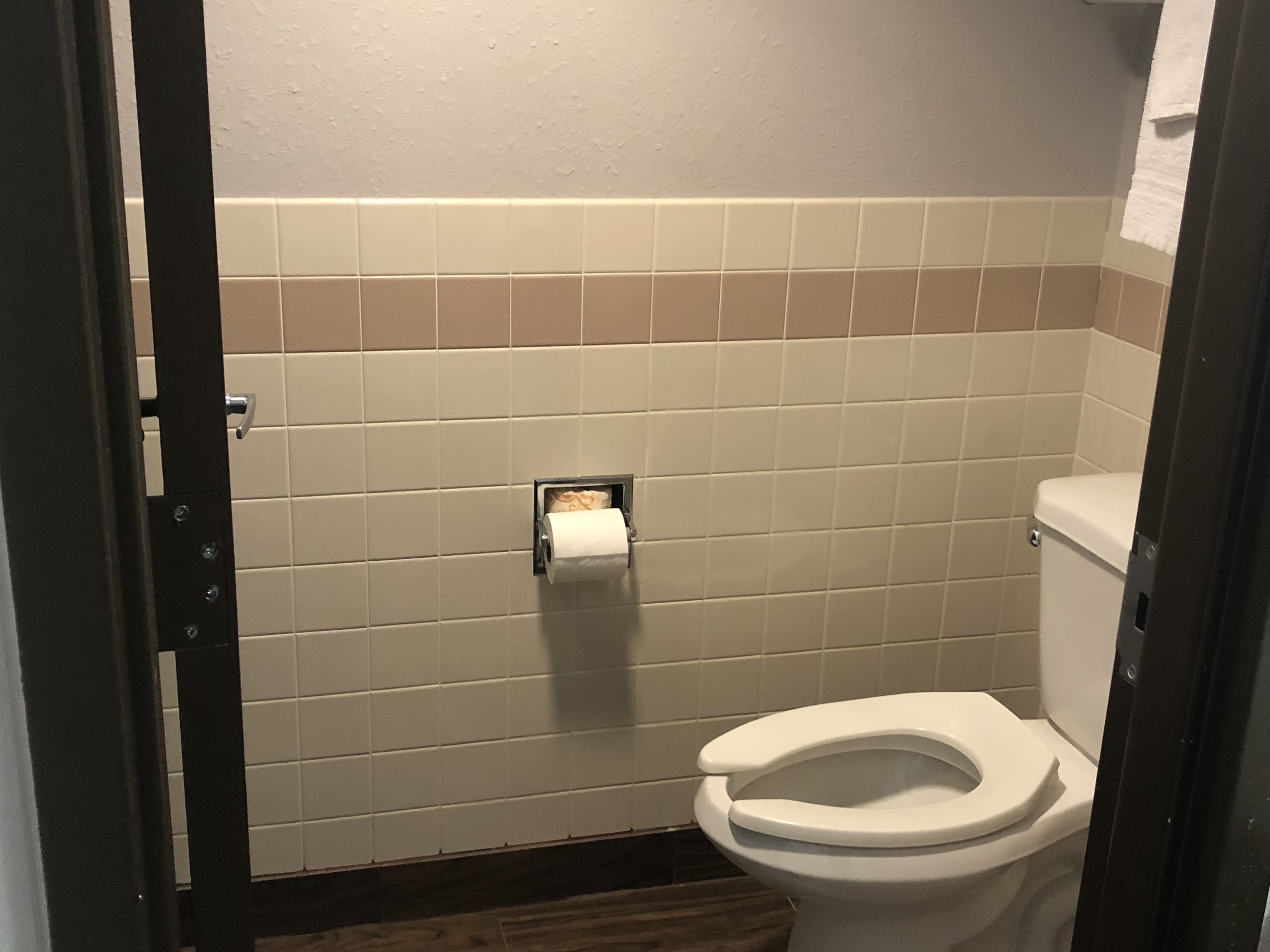 A bathroom with a toilet, a paper towel dispenser, and a tiled wall.