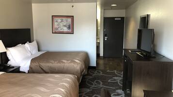 A hotel room with two beds, a desk with a TV, and a door leading to a bathroom.