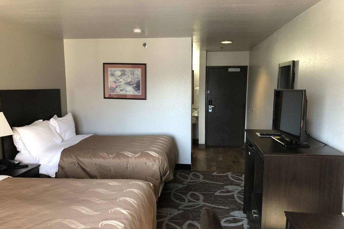 A hotel room with two beds, a desk with a TV, a framed picture on the wall, and a door leading to a bathroom.