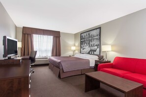 Ein Hotelzimmer mit einem Bett, einem Schreibtisch mit Computer, einem roten Sofa und einem Bild an der Wand.