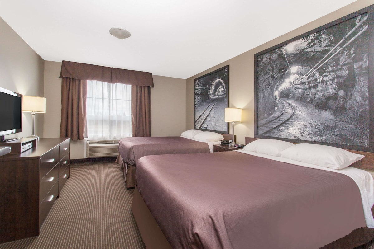 Ein Hotelzimmer mit zwei Betten, einem Fernseher, einem Schreibtisch und einem großen Bild in einem Rahmen an der Wand.
