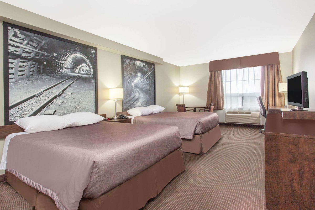 Ein Hotelzimmer mit zwei Betten, einem Fernseher, einem Schreibtisch und einem großen Gemälde eines Tunnels.