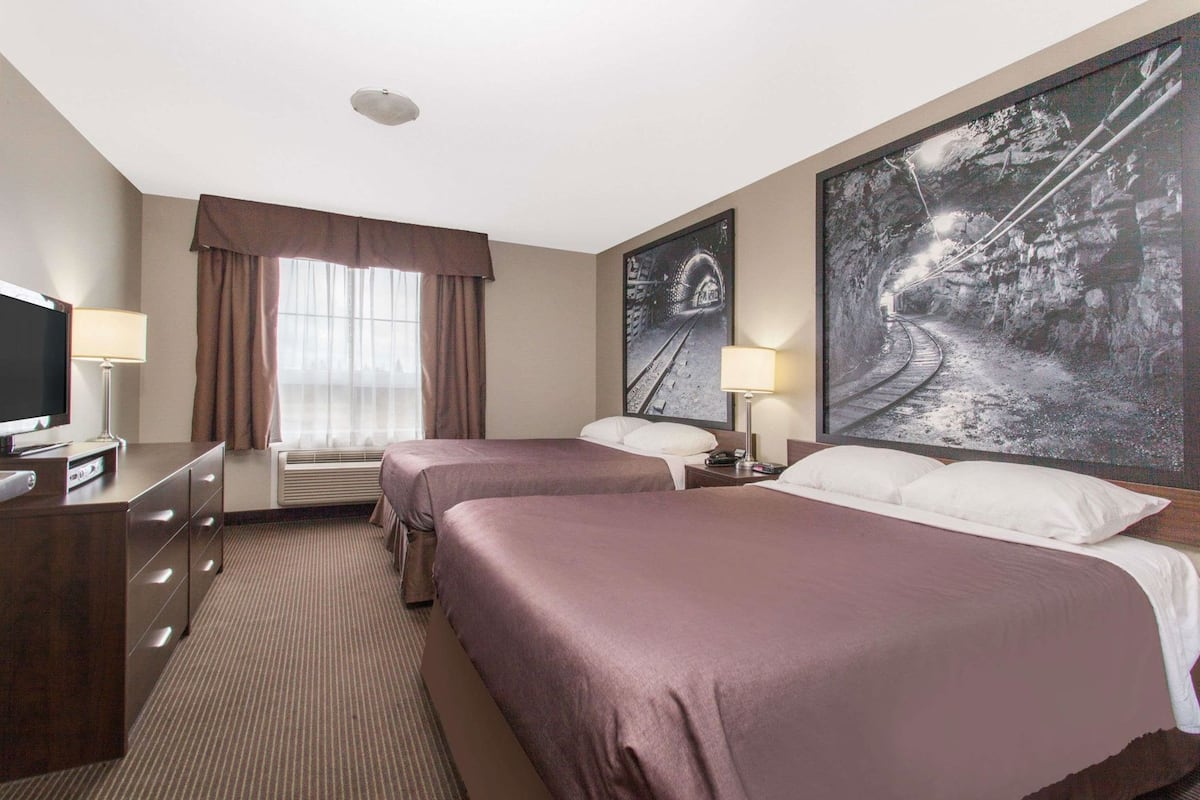 Ein Hotelzimmer mit zwei Betten, einem Schreibtisch, einem Fernseher und einem großen Fenster mit Vorhängen.