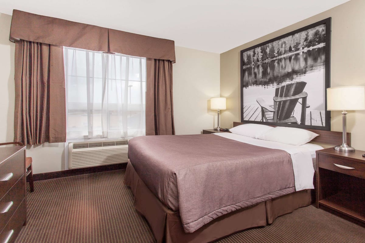 Ein Hotelzimmer mit einem großen Bett, zwei Nachttischlampen, einem Sessel, einem Schreibtisch und einem fenster mit Vorhängen.