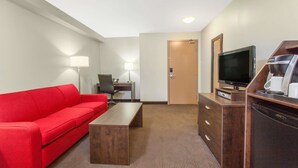 Ein Hotelzimmer mit einem roten Sofa, einem Holztisch, einem Fernseher auf einem Holzständer, einem Schreibtisch mit einer Lampe und einer Minibar.