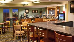 A hotel kitchen with a central island, wooden chairs, a clock on the wall, and a refrigerator. - AmericInn by Wyndham Osage (Osage)
