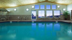 An indoor swimming pool with clear blue water, surrounded by lounge chairs and large windows. - AmericInn by Wyndham Osage (Osage)