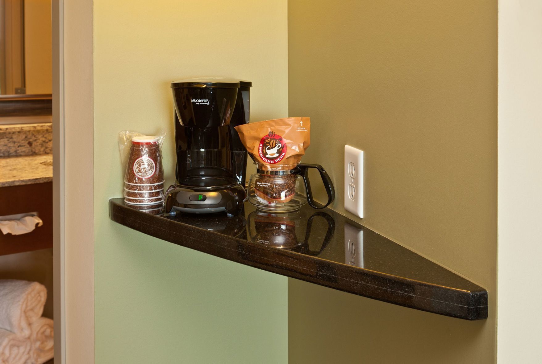 A kitchen counter with a coffee maker, a bag of coffee pods, and a glass jar of coffee beans.