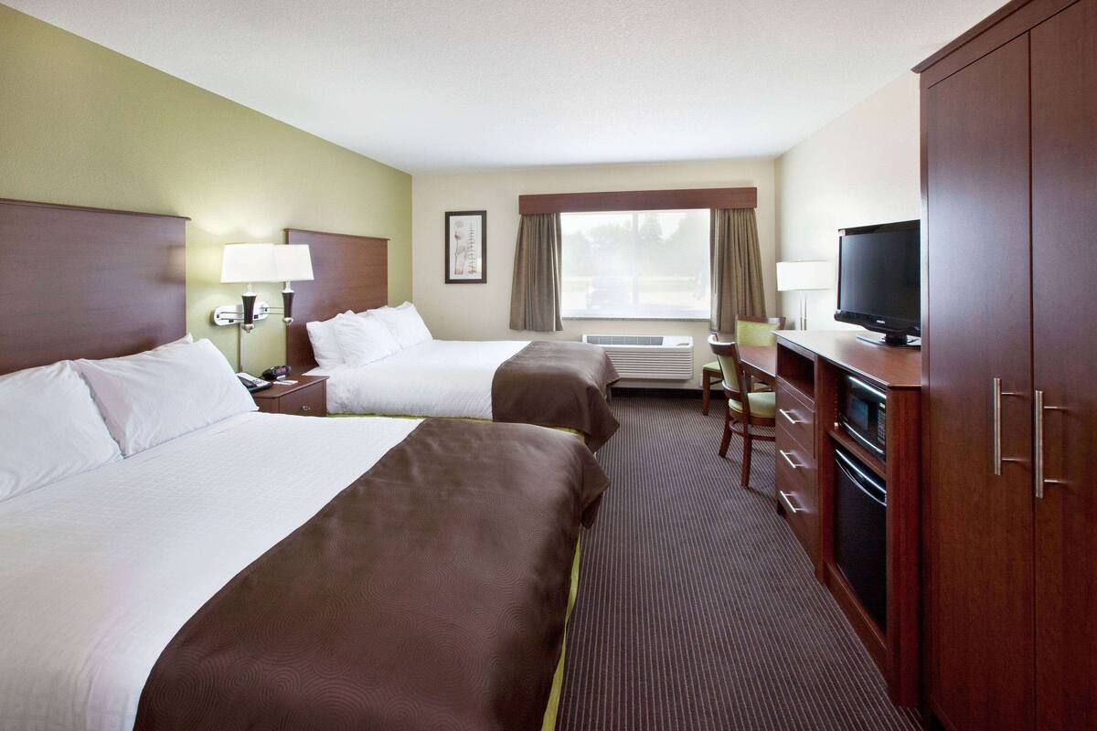 Une chambre d’hôtel avec deux lits, une télévision, un bureau avec une chaise et une armoire.
