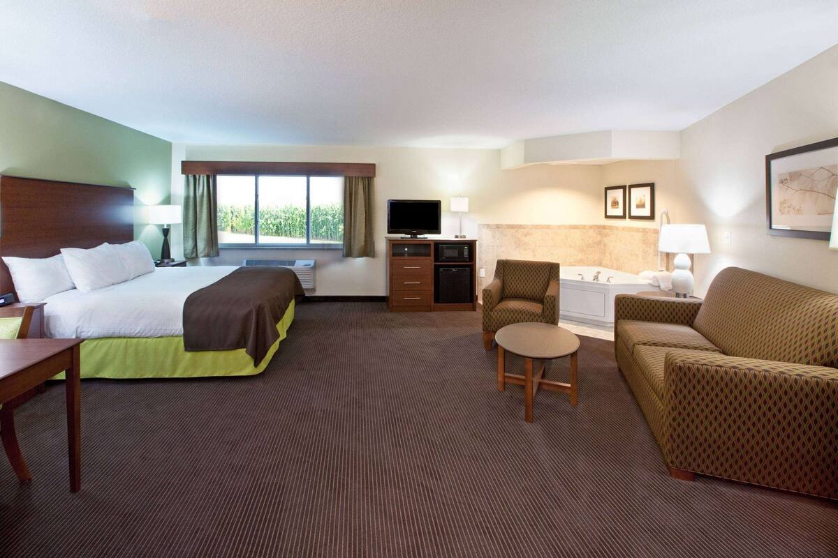 Une chambre d’hôtel comprenant un lit, un bureau, une chaise, un canapé, une télévision, un four à micro-ondes, une petite table et une salle de bain avec une baignoire et un lavabo.