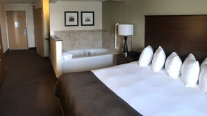 A hotel room with a large bed, a separate bathroom with a bathtub, a desk, and two framed pictures on the wall. - AmericInn by Wyndham Osage (Osage)