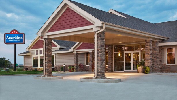 A hotel with a covered entrance, brick pillars, and a sign indicating it is an American Inn. - AmericInn by Wyndham Osage (Osage)