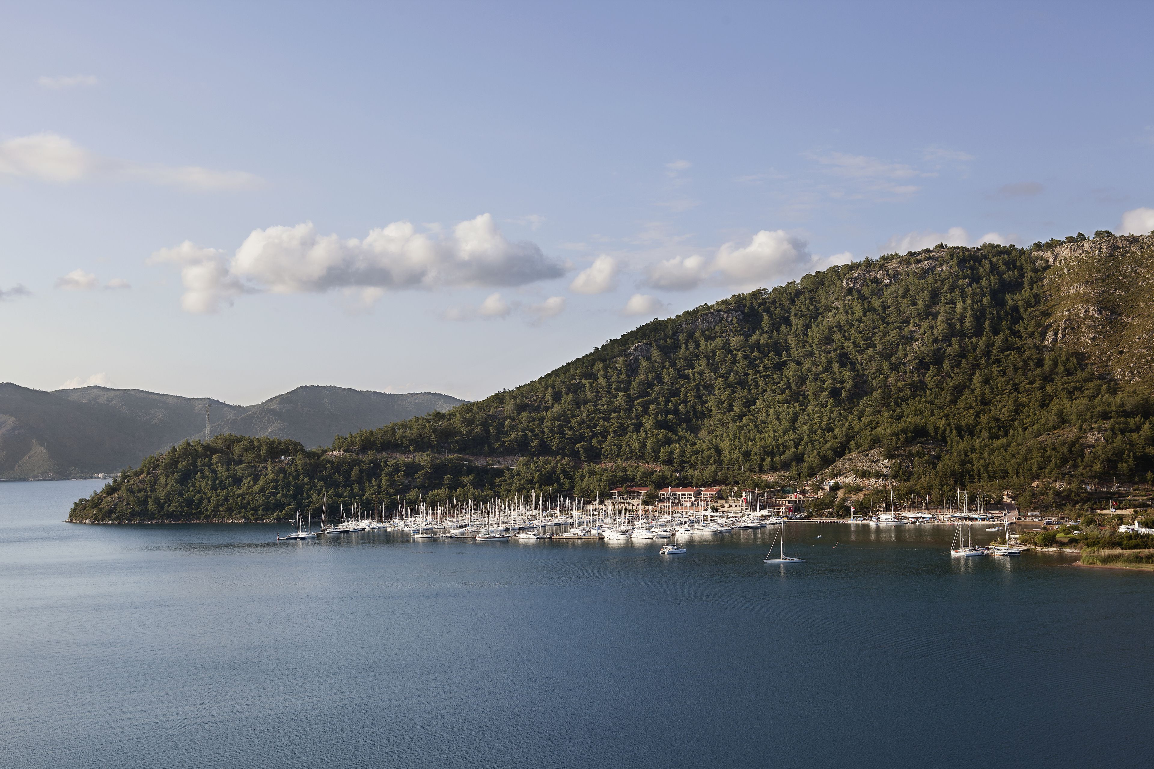 A marina with numerous boats docked, surrounded by a mountainous landscape and a clear sky.
