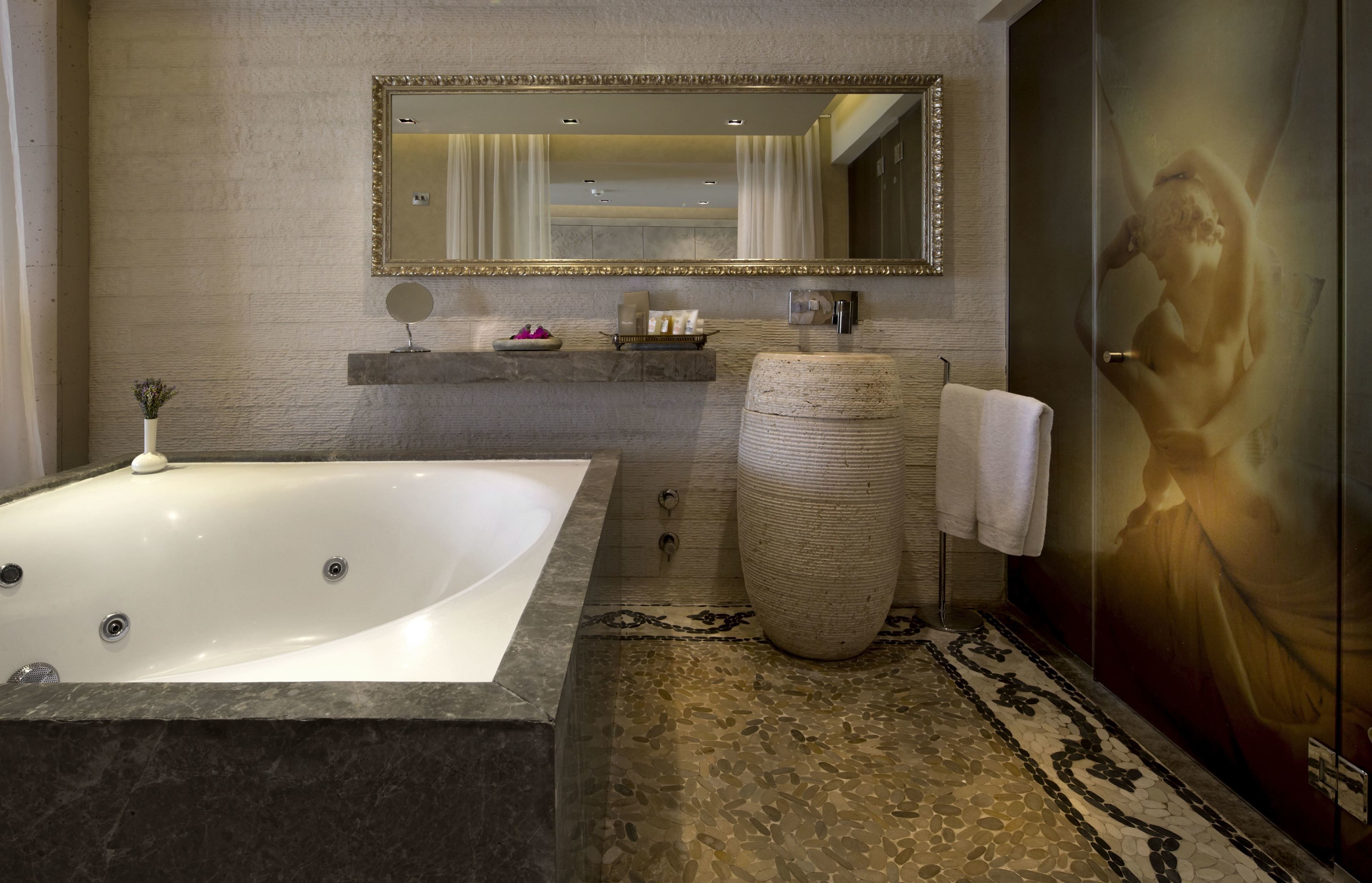 A modern bathroom with a large bathtub, a round stone sink, and a mirror above the sink.