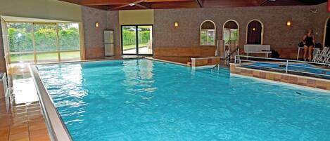An indoor swimming pool with clear water, tiled floor, and a brick wall.