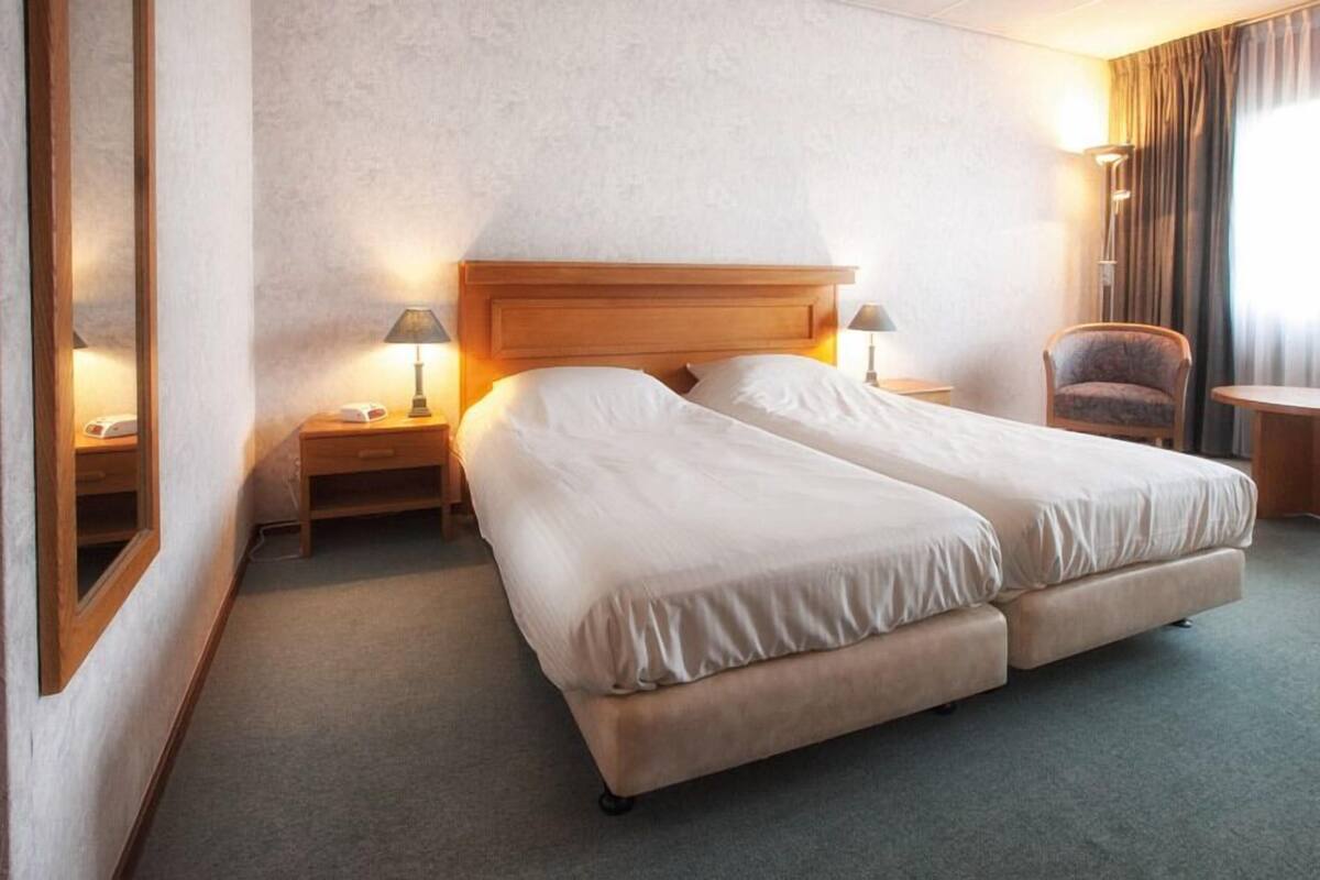 Ein Hotelzimmer mit einem Doppelbett, zwei Nachttischen mit Lampen, einem Sessel und einem kleinen Tisch.