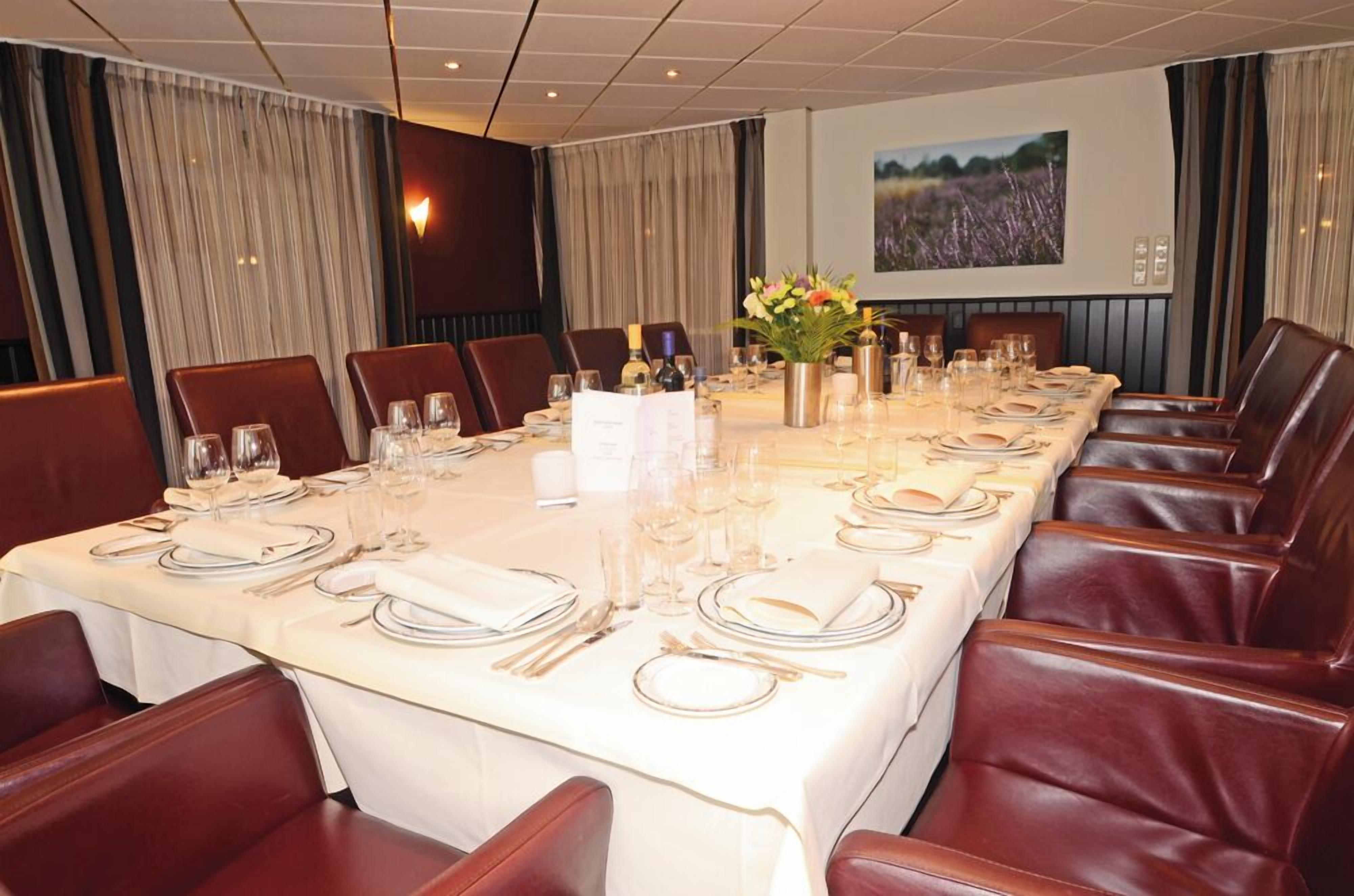 A conference room with a long table set for a formal meeting, surrounded by leather chairs.