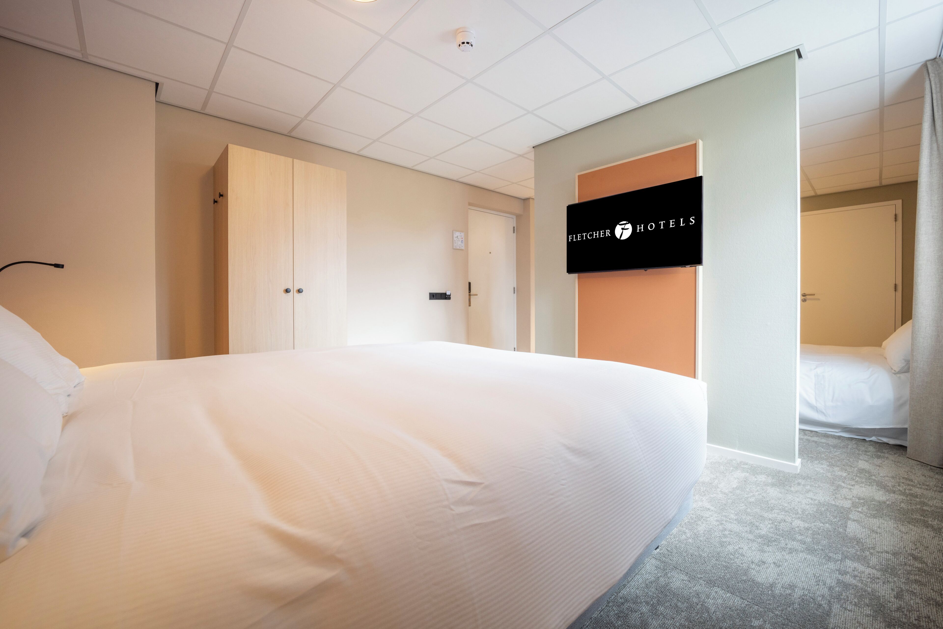 Habitación de hotel con una cama grande, un armario, una puerta y un cartel de Fletcher Hotels.