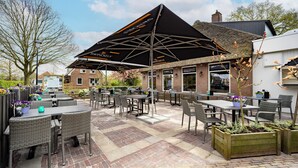 An outdoor patio area with tables and chairs, a large black umbrella, and brick flooring.