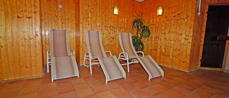A room with wooden panel walls, a tiled floor, and four reclining chairs with striped cushions.