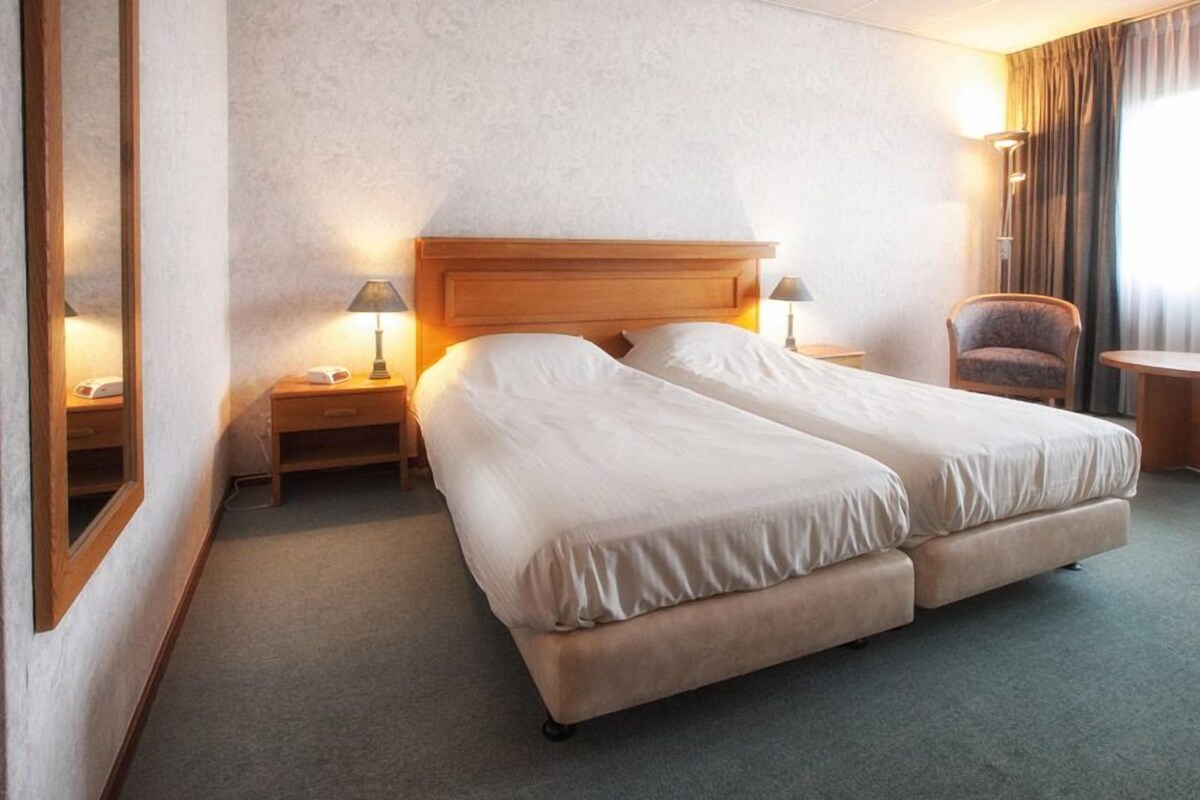 A hotel room with a double bed, two bedside tables with lamps, a chair, and a small table.