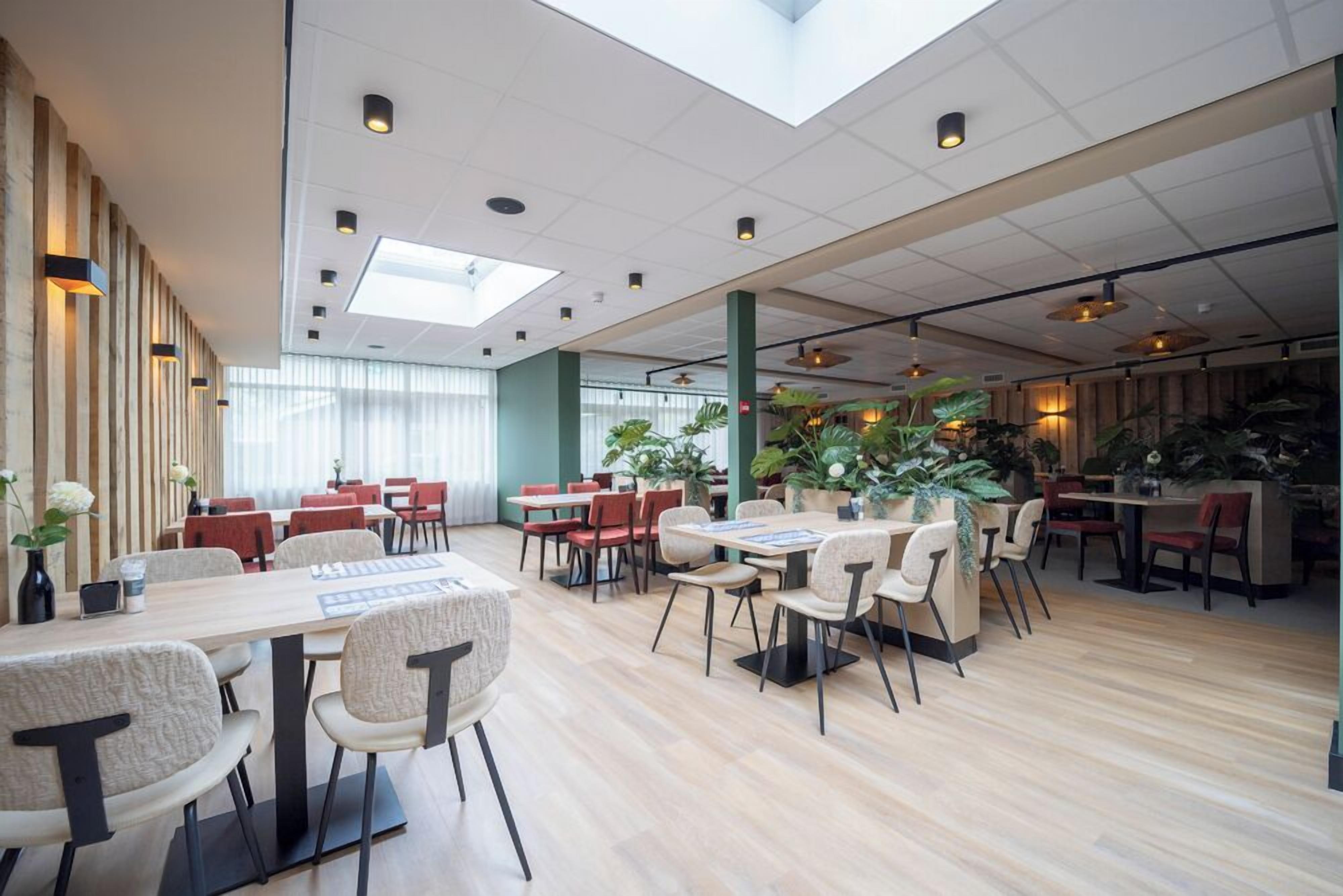 A spacious indoor area with multiple tables and chairs, a high ceiling with skylights, and potted plants.